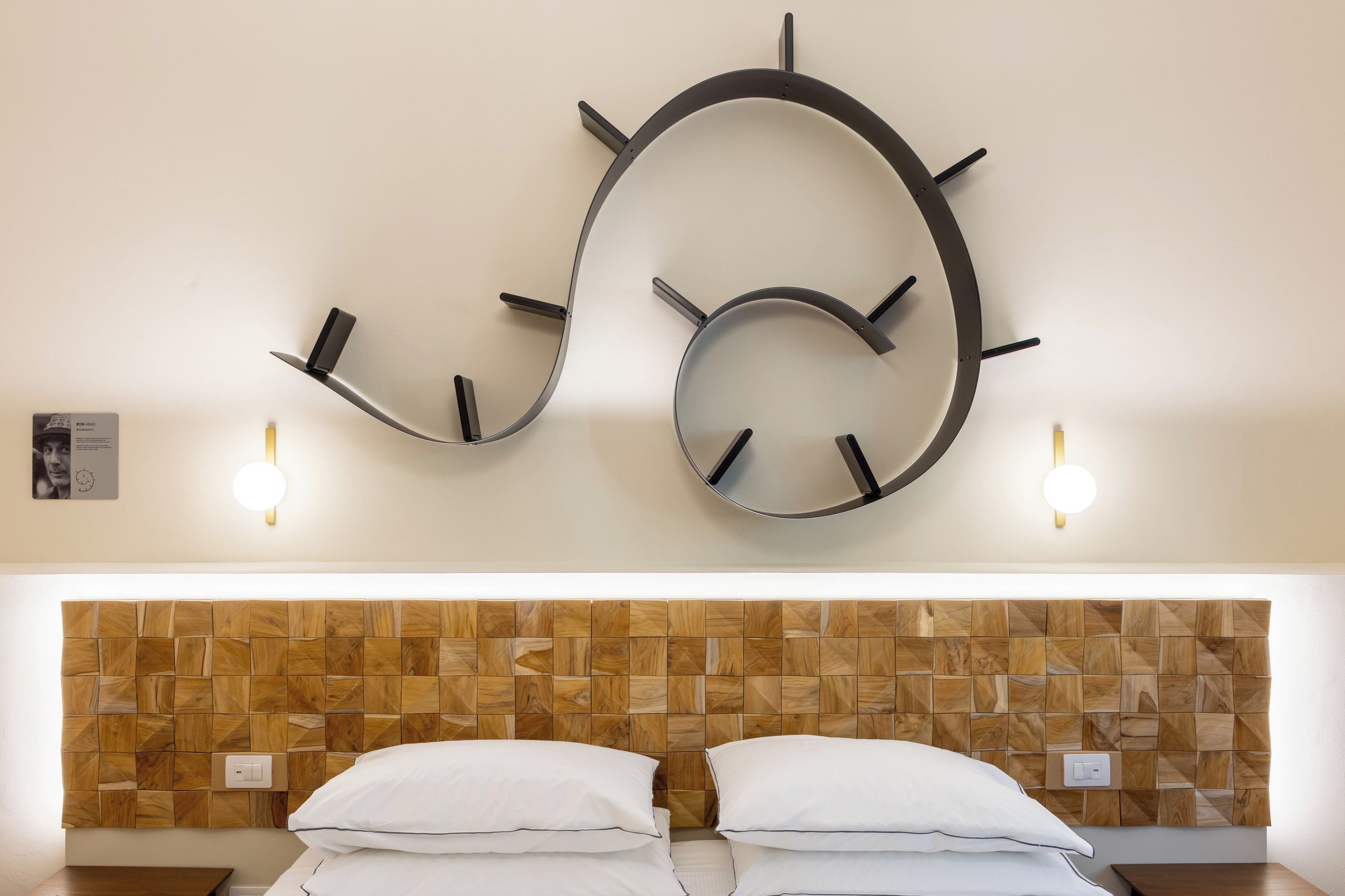 Ein modernes Hotelzimmer mit einer einzigartigen, gebogenen Wanduhr, einem Holz-Kopfteil und zwei Nachttischen.
