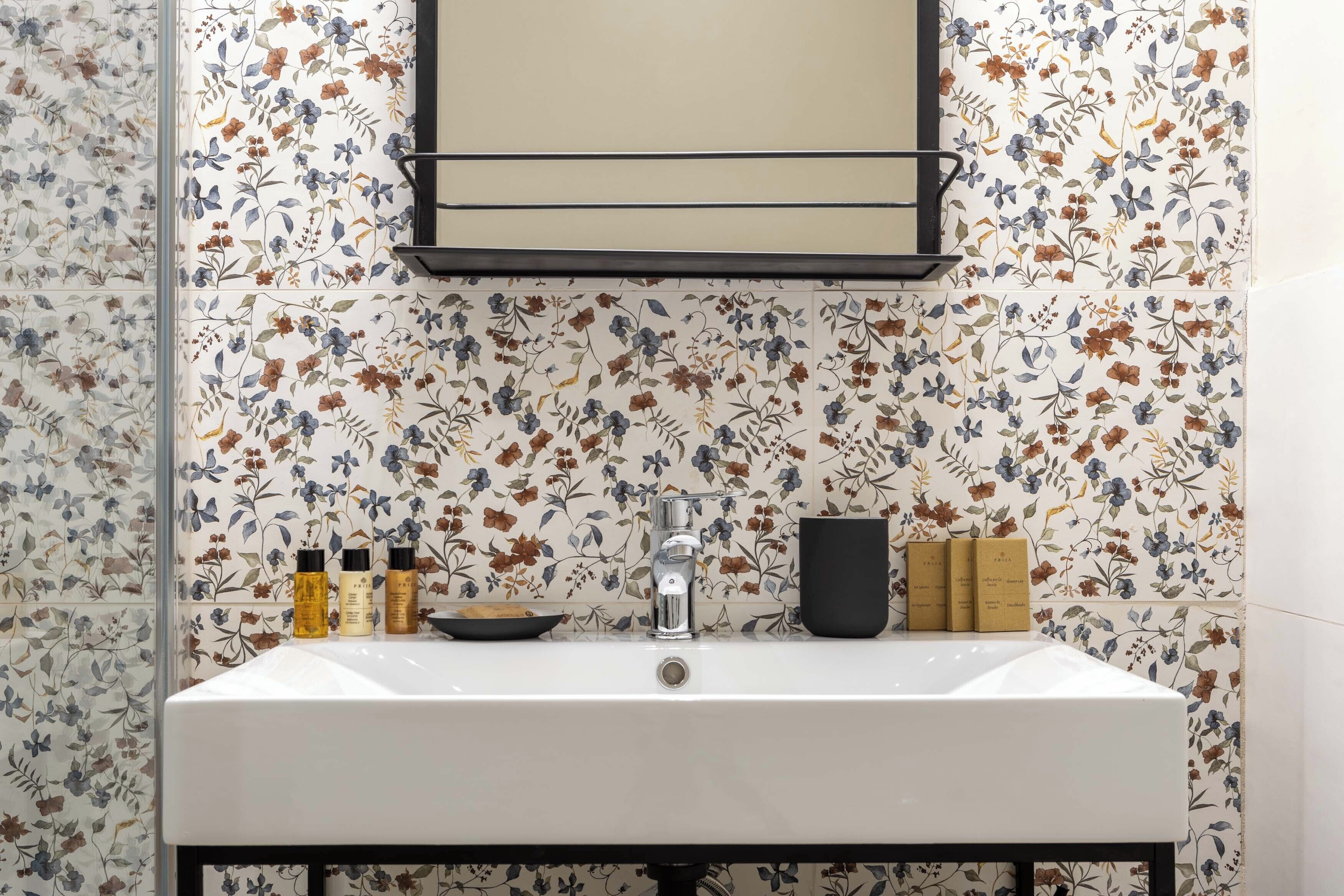 A bathroom with a white sink, a mirror, and floral-patterned tiles.