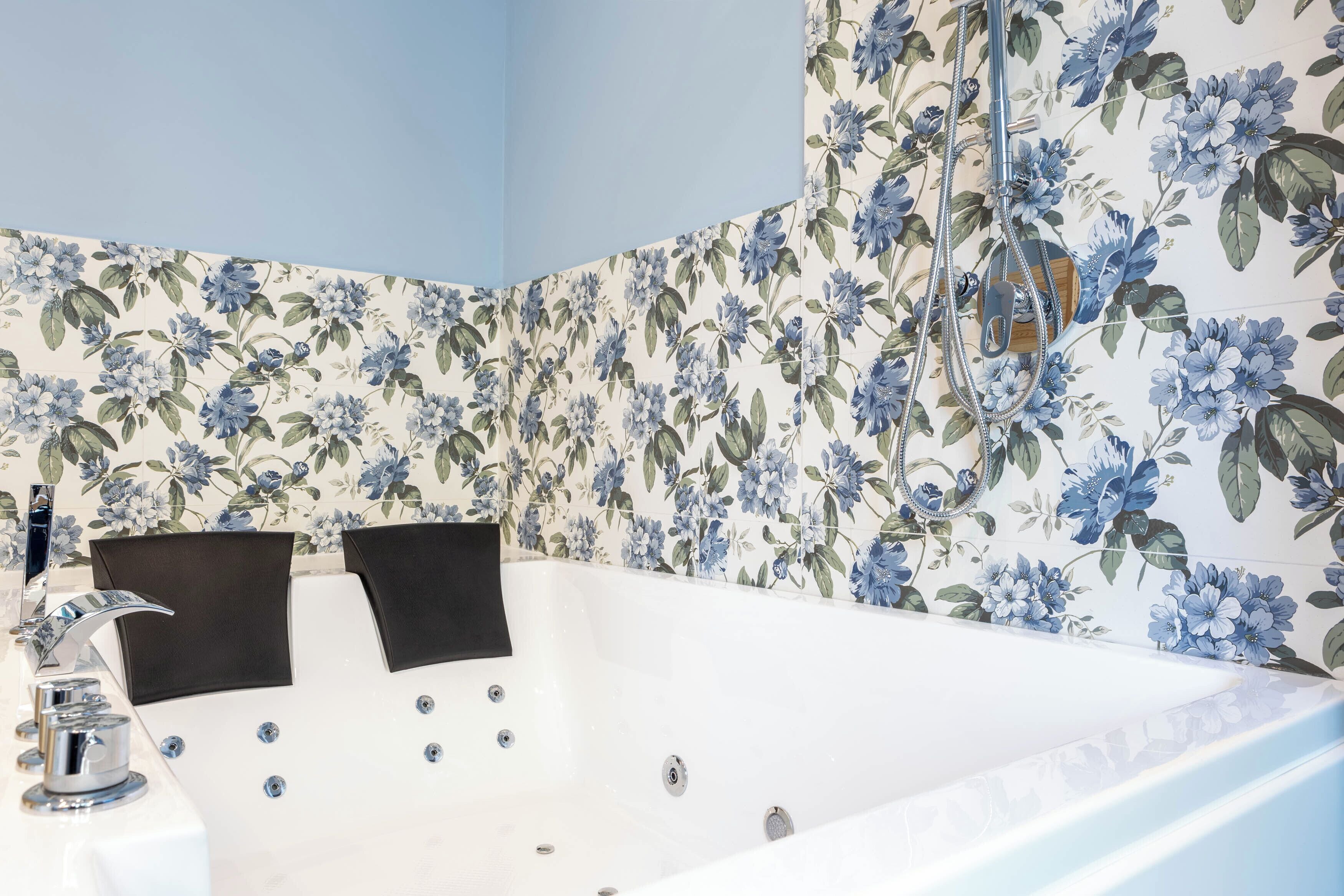 Un bagno con una vasca da bagno ampia, una doccia e un water. Le pareti sono decorate con un motivo floreale.