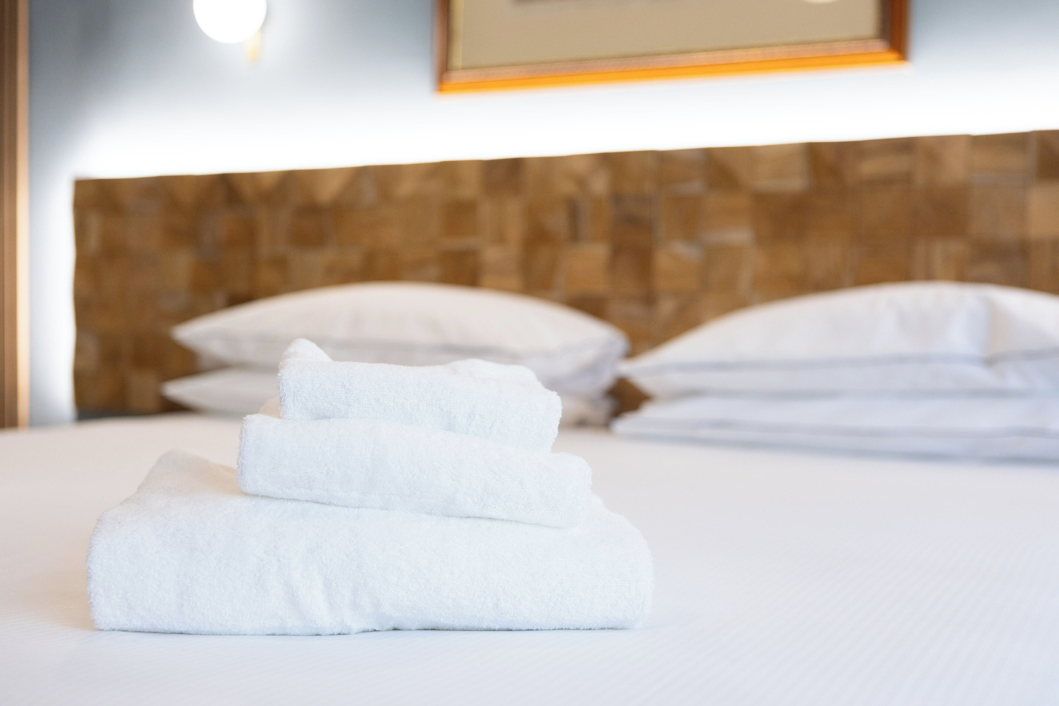 A neatly made bed with white pillows and a stack of folded white towels.