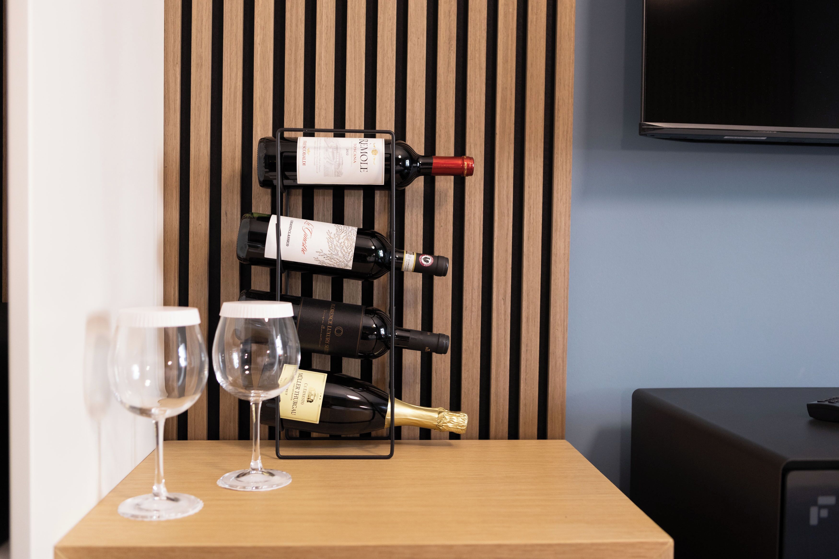 Una mesa de madera con dos copas de vino y tres botellas de vino en una estantería.