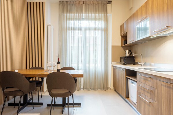 A modern kitchen with wooden cabinets, a dining table with chairs, and a window with sheer curtains. - Pier Capponi 17 Room & Suites (Florence)