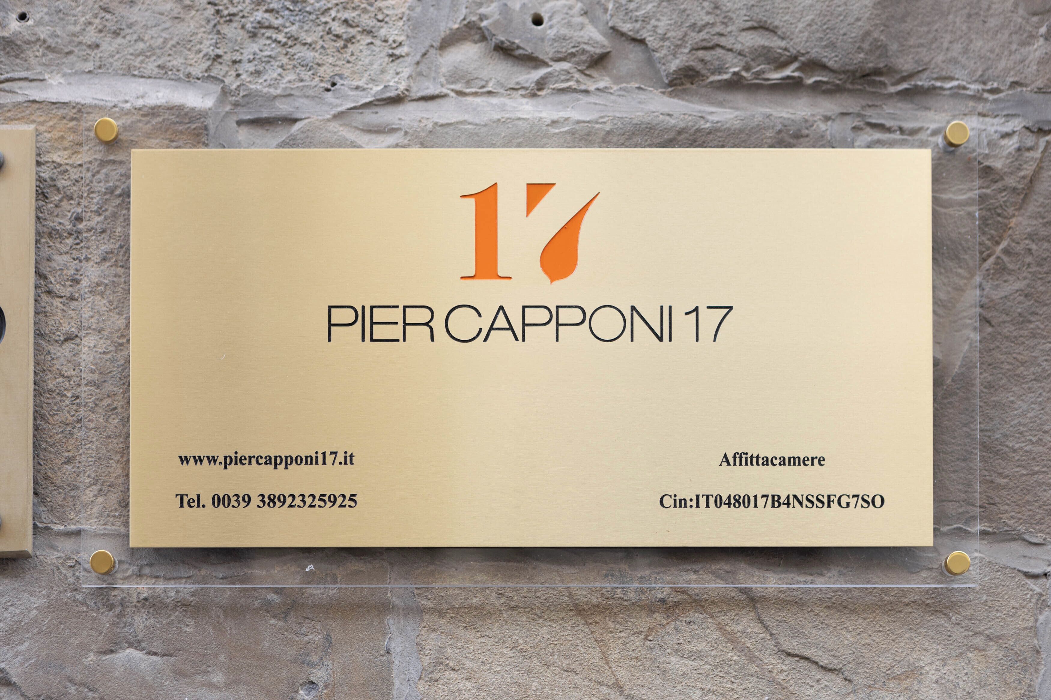 Een visitekaartje met het nummer 17, de naam 'PIER CAPONI 17', een website, telefoonnummer en adres, vastgepind aan een stenen muur.