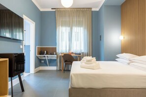 Habitación de hotel con cama, escritorio, silla, televisión y ventana con cortinas.