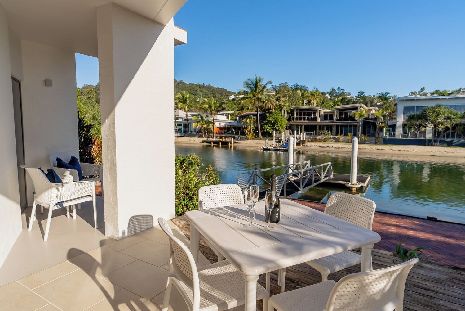 A terrace with a table and chairs, overlooking a marina with boats and houses.