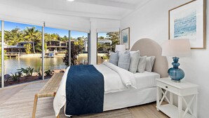 Ein Schlafzimmer mit Bett, Nachttisch, Lampe und Blick auf ein Gewässer sowie Gebäude.