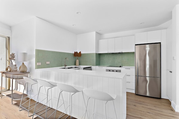 Una cocina moderna con armarios blancos, un refrigerador de acero inoxidable y un salpicadero de azulejos verdes.