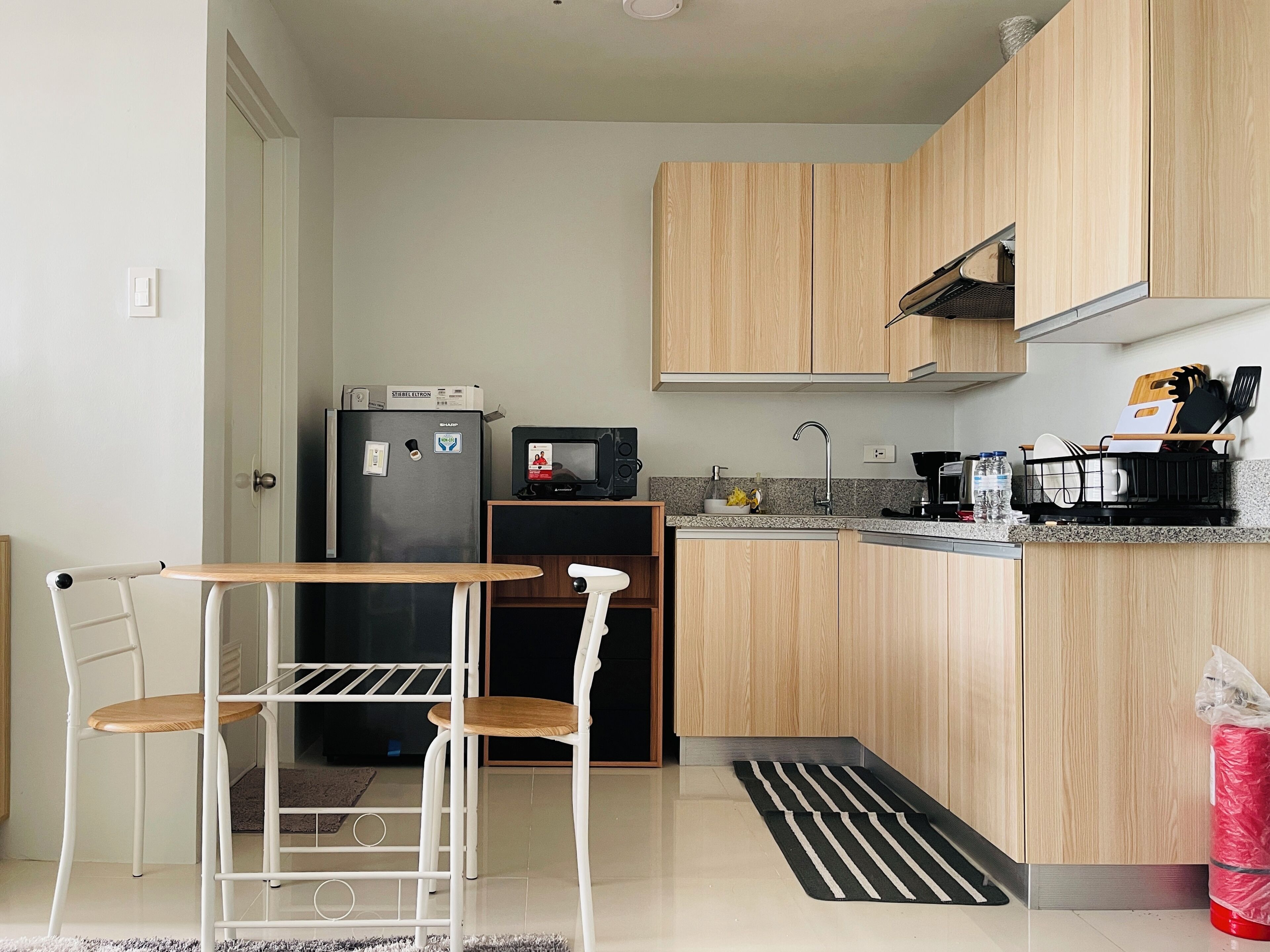 A compact kitchen with wooden cabinets, a refrigerator, a microwave, and a small dining area with a table and chairs.