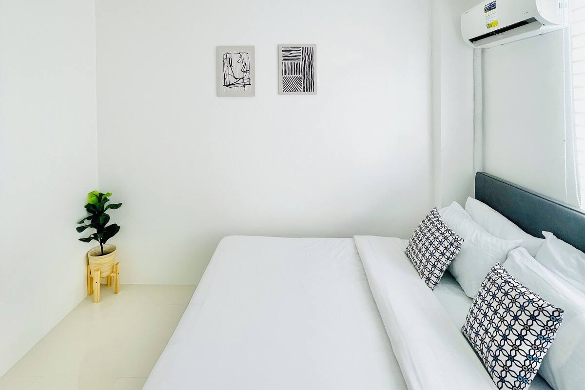 A minimalist hotel room with a large bed, a small plant, and two wall art pieces.