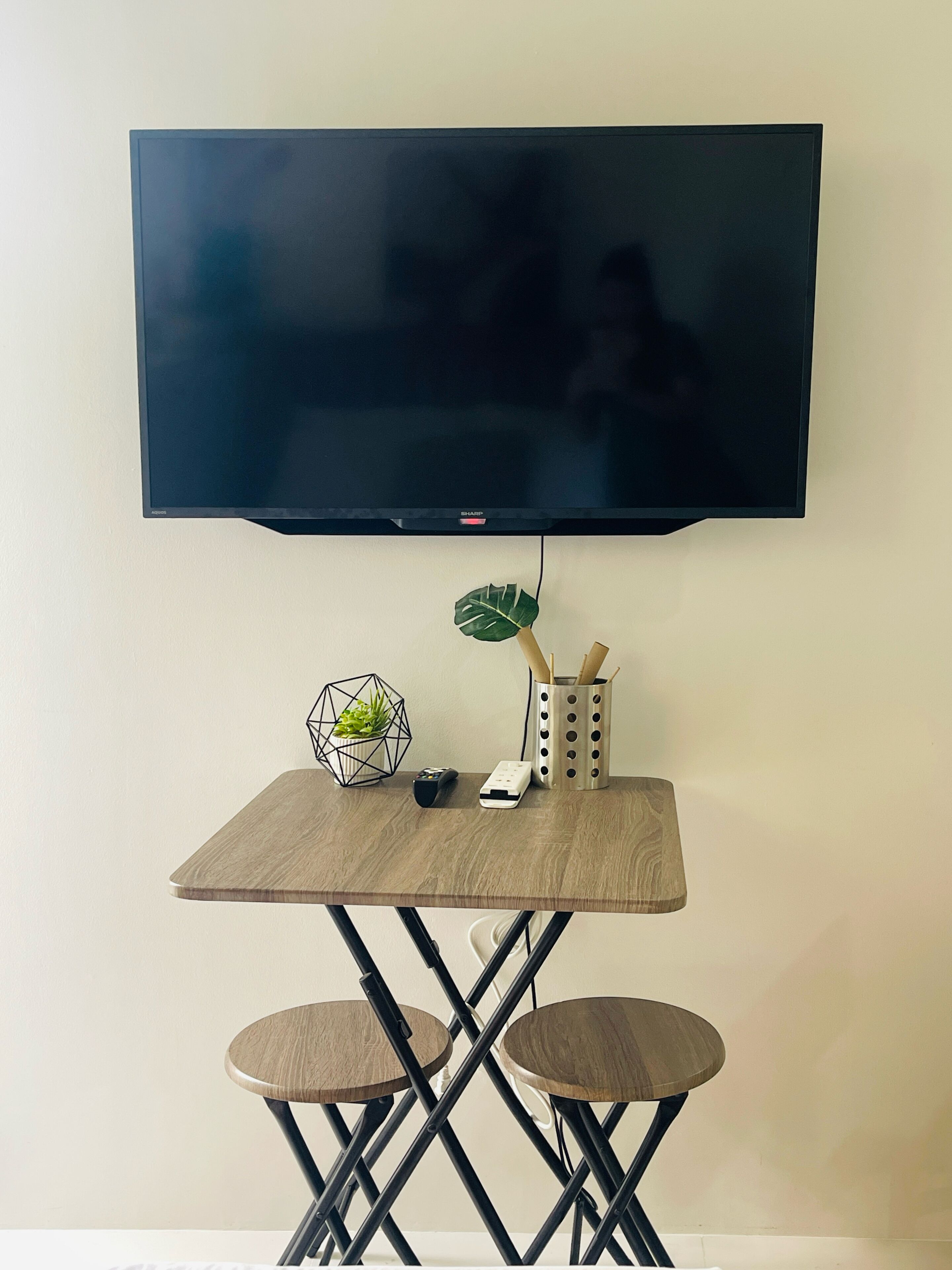 A flat-screen TV mounted on a wall above a wooden table with two chairs.