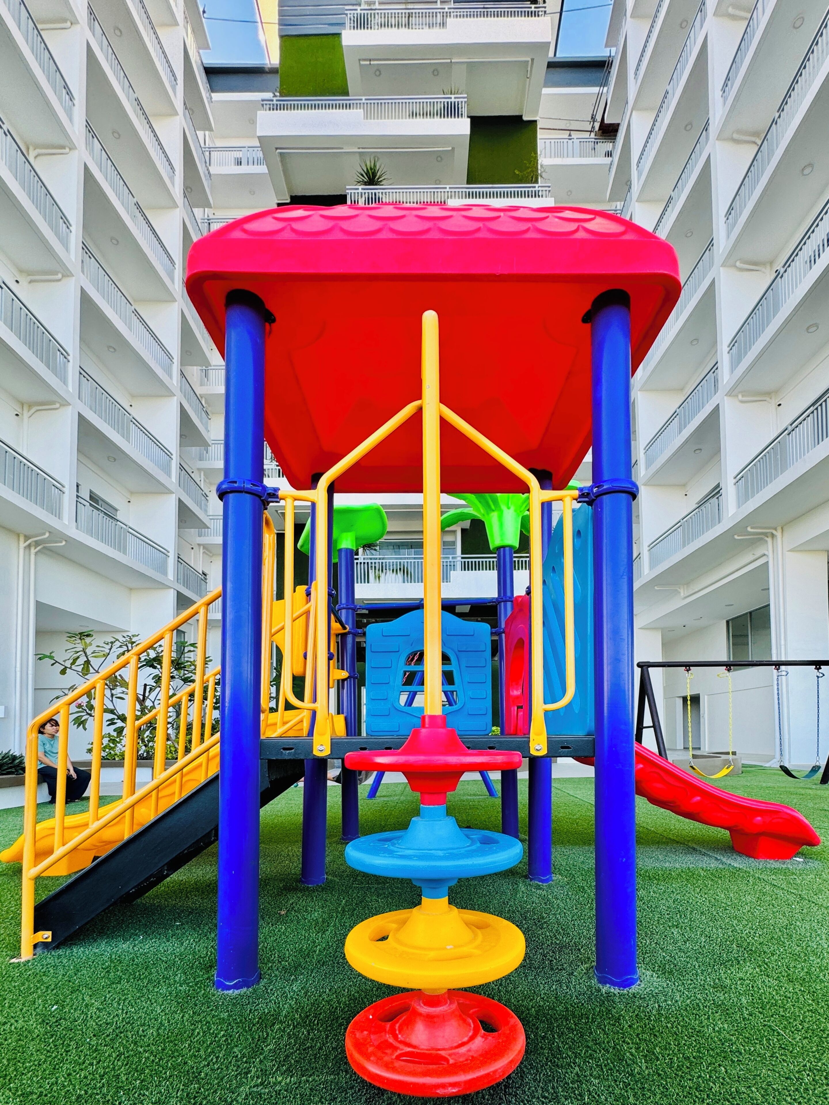 Un terrain de jeux équipé d’un toboggan et de structures d’escalade, entouré d’un bâtiment doté de balcons et d’un toit végétalisé.