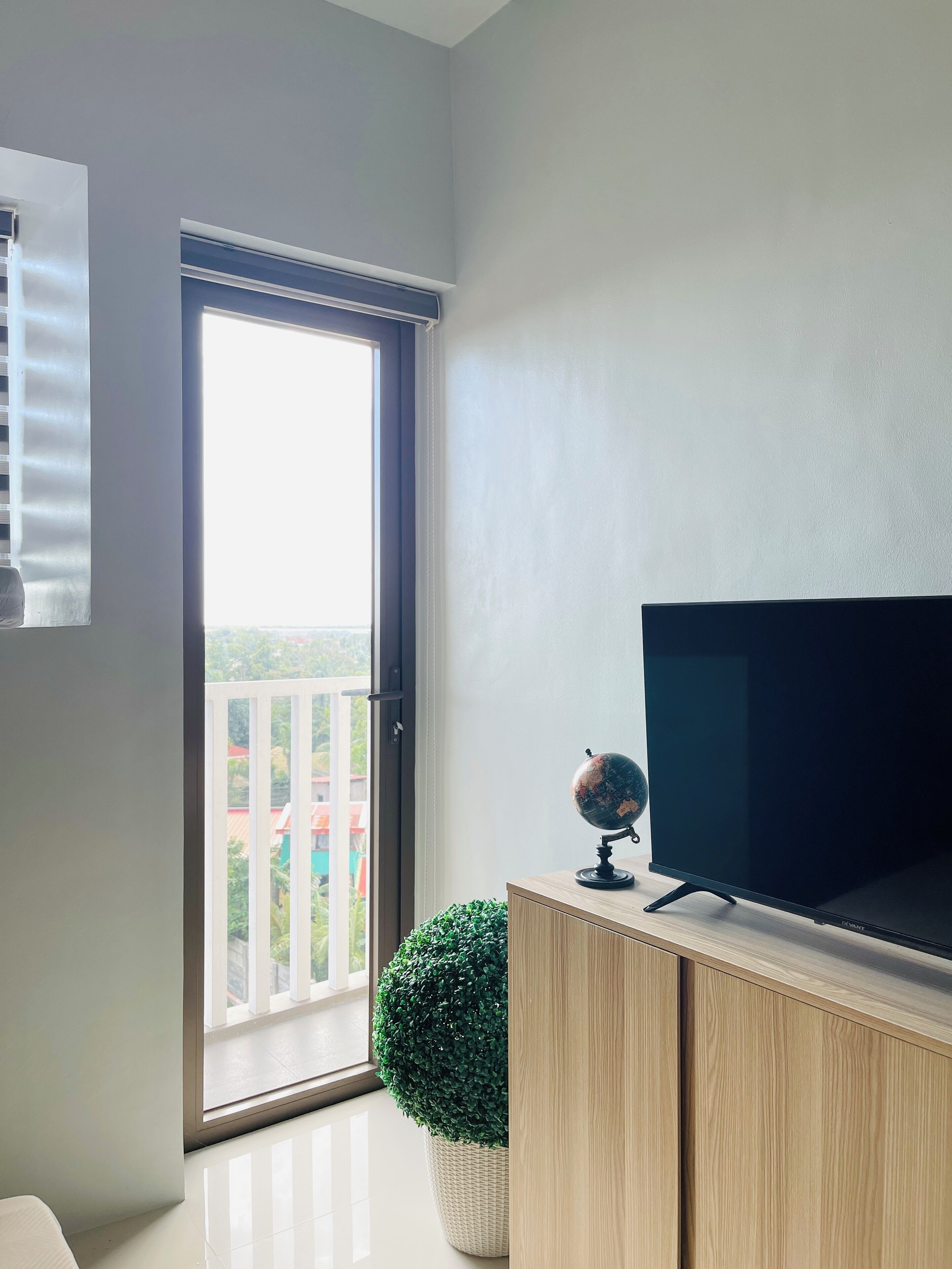 A room with a large window, a flat-screen TV on a wooden stand, a globe, and a potted plant.