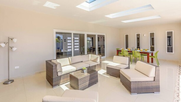 A spacious living area with a sofa set, a dining table with chairs, and a large sliding glass door leading to an outdoor area.