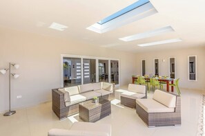 A spacious living area with a sofa set, a dining table with chairs, and a large sliding glass door leading to an outdoor area.