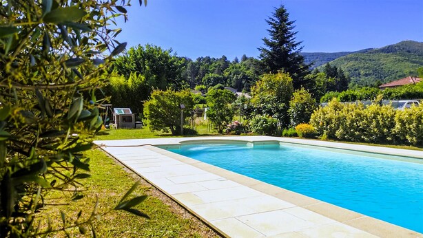 A rectangular swimming pool with a tiled edge, surrounded by well-maintained grass and various shrubs.