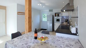 A modern kitchen with a refrigerator, microwave, and stove. There is a dining table with a bottle and a bowl of fruit.
