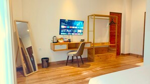 Een moderne kamer met een houten bureau, een stoel, een bed, een aan de muur bevestigde televisie en een spiegel.
