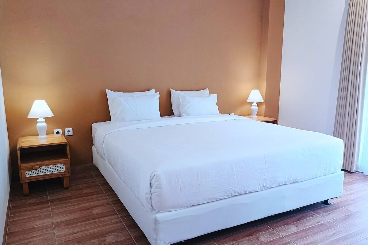Une chambre d’hôtel avec un grand lit, deux tables de chevet avec des lampes et une table de nuit en bois.