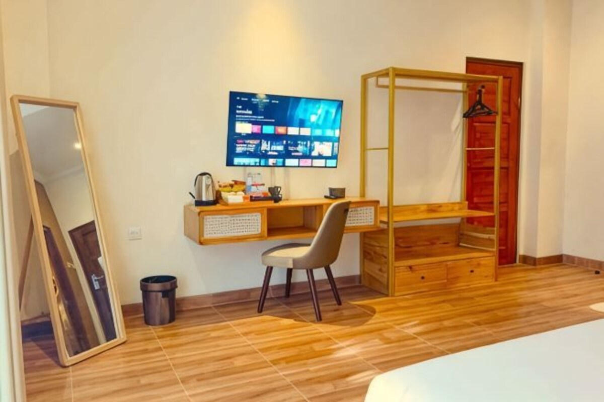 A room with a wooden desk, a chair, a bed, a TV mounted on the wall, and a wardrobe.