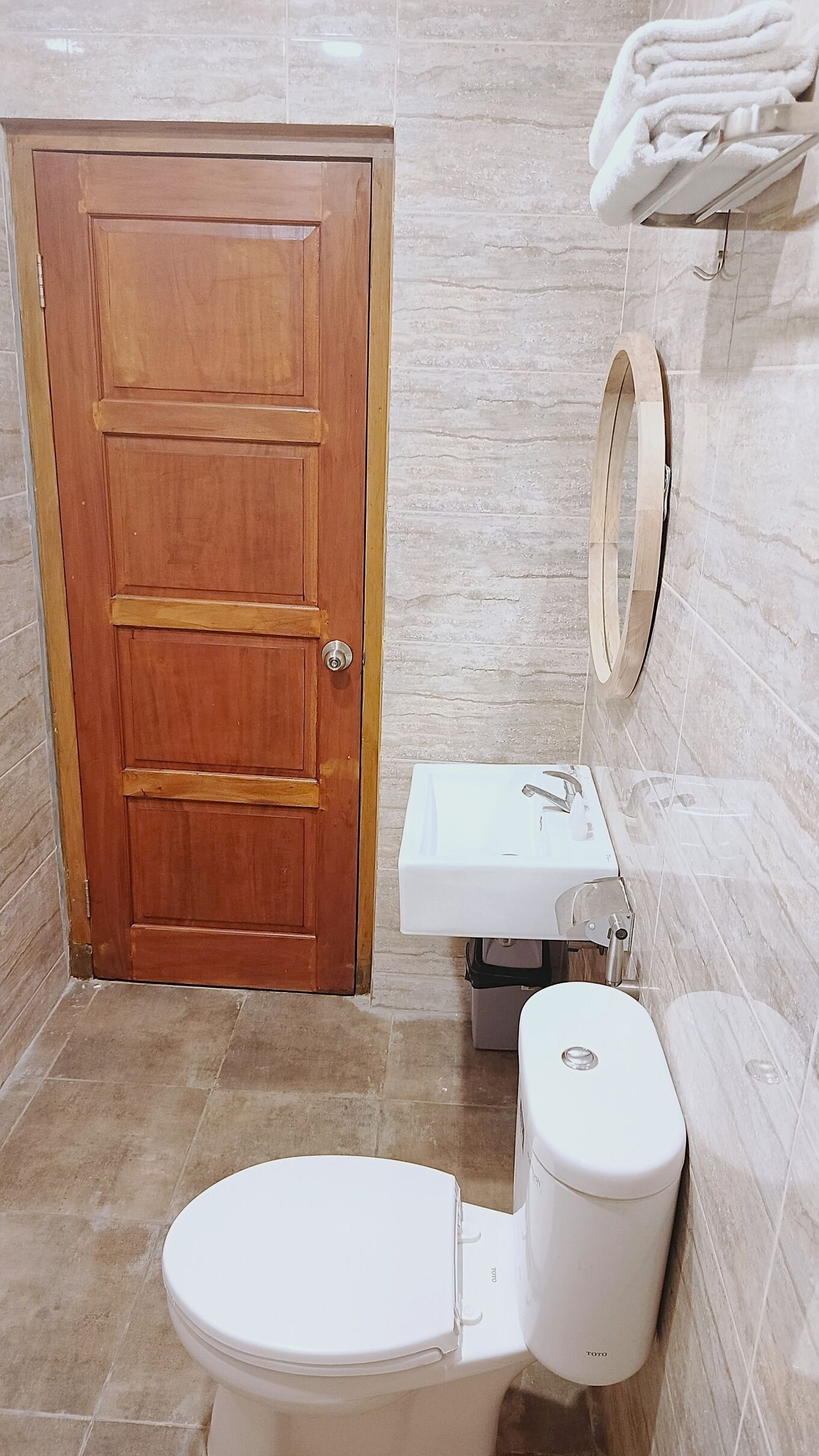 A bathroom with a wooden door, a white toilet, a sink with a mirror, and a towel rack.