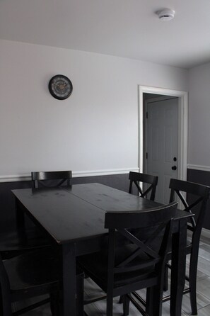 A dining area with a dark wooden table and chairs, a wall clock, and a door.