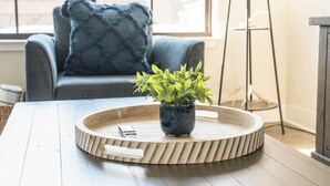 A round wooden tray with a potted plant on a table, a remote control, and a grey sofa with a blue pillow in the background.