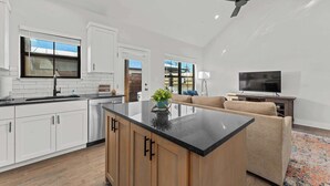 A modern kitchen with white cabinets, a black countertop island, and a ceiling fan.