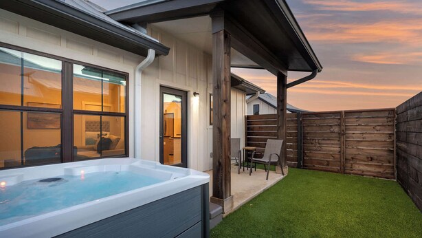 A backyard with a hot tub, a wooden fence, and a patio with chairs.