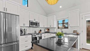 A modern kitchen with white cabinets, stainless steel appliances, a large island, and a view of the outdoors.