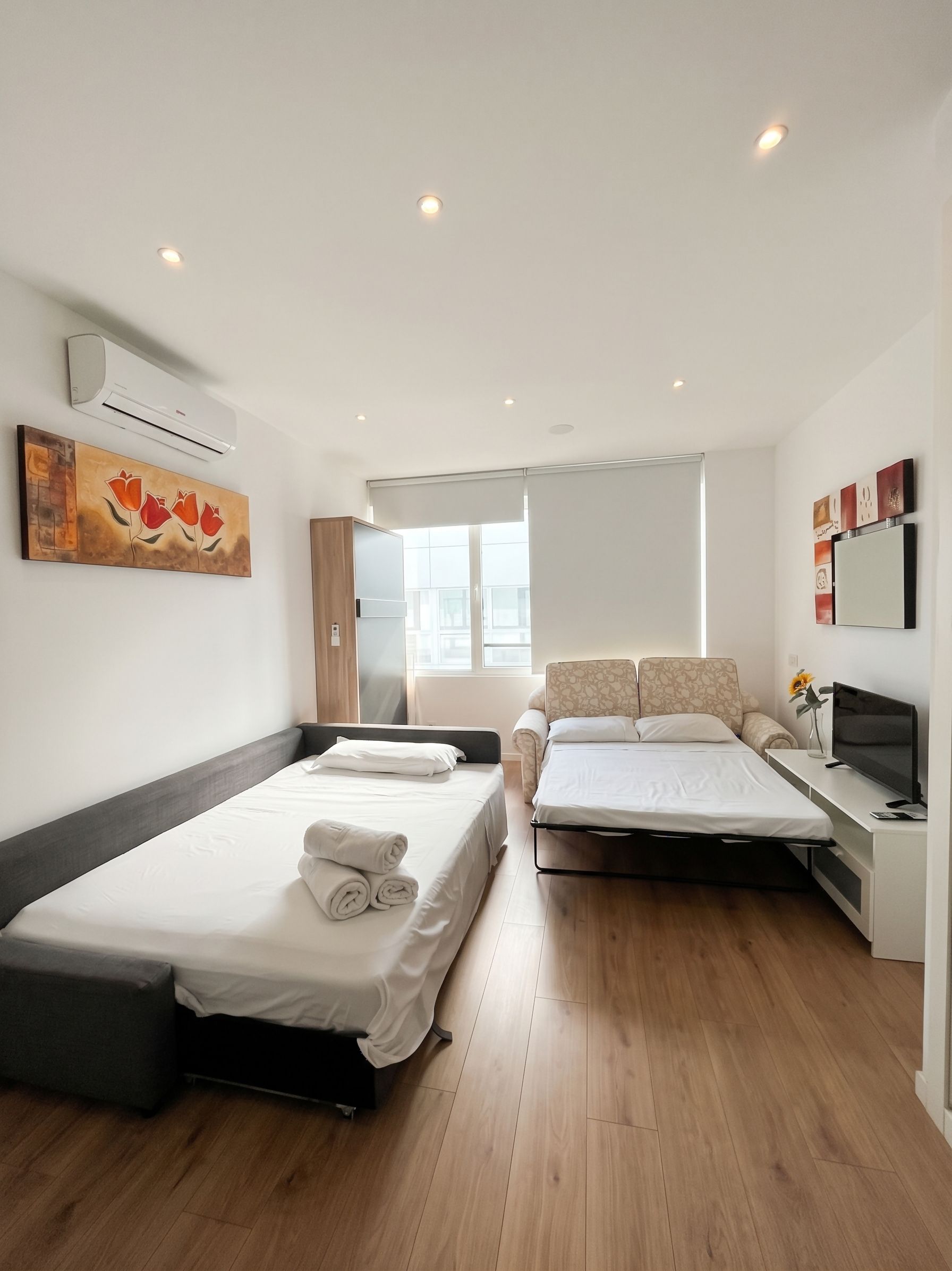 A modern hotel room with a bed, a sofa bed, a desk with a TV, and a window.