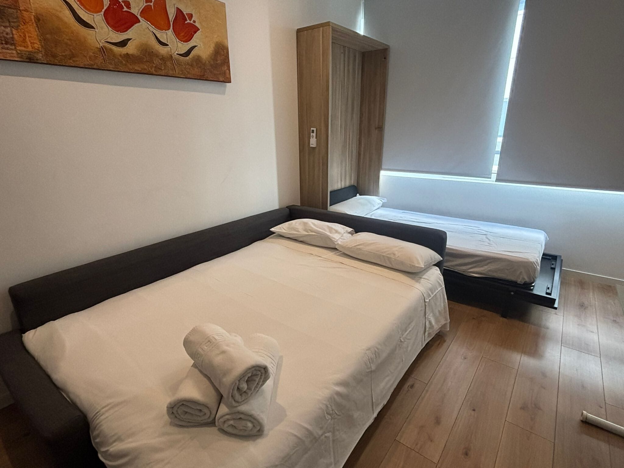 Cama doble con sábanas blancas y toallas enrolladas, un armario de madera y una ventana con cortinas.