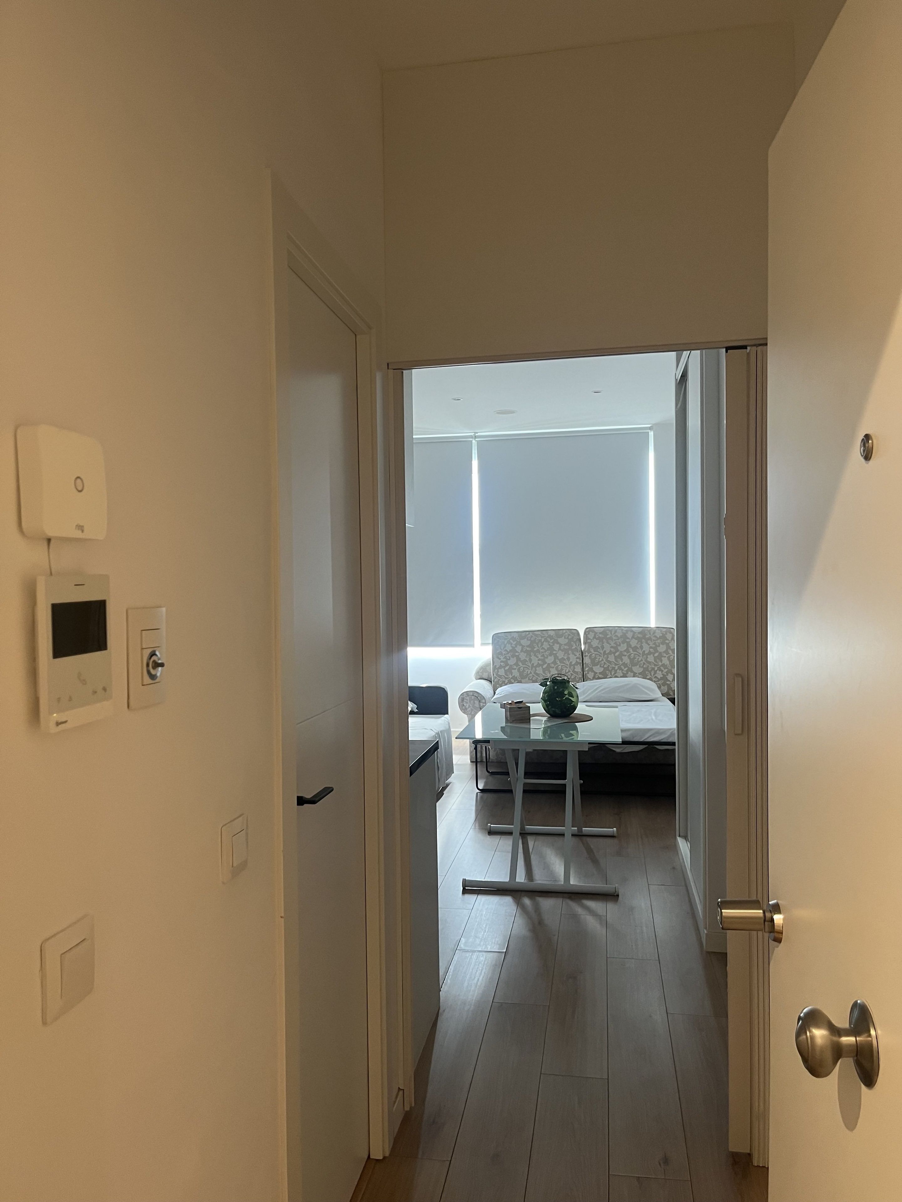 Un pasillo que conduce a un dormitorio con cama, mesita de noche y ventana.