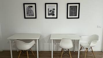 A room with a white table and two white chairs with wooden legs, a white floor, and three framed artworks on the wall.