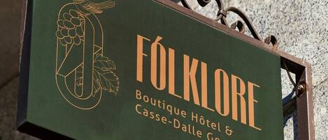 Une enseigne pour le «
FOLKLORE Boutique Hotel & Casse-Dalle Gourmand
», avec une illustration représentant un oiseau et des raisins.