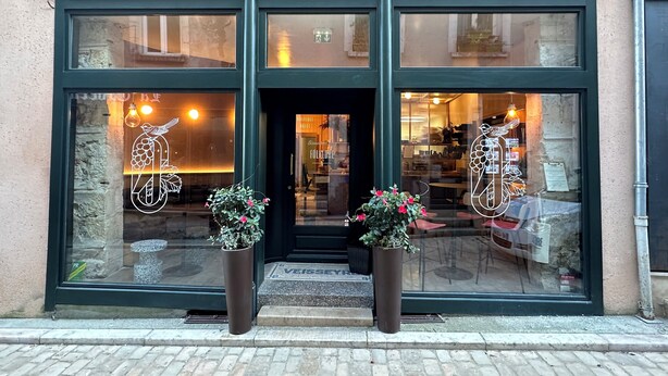 The entrance of Boutique Hotel & Casse-Dalle Gourmand Folklore with a large glass window displaying a bird and fruit design, two potted plants, and a visible entrance door. - FÓLKLORE BOUTIQUE HOTEL (Sancerre)