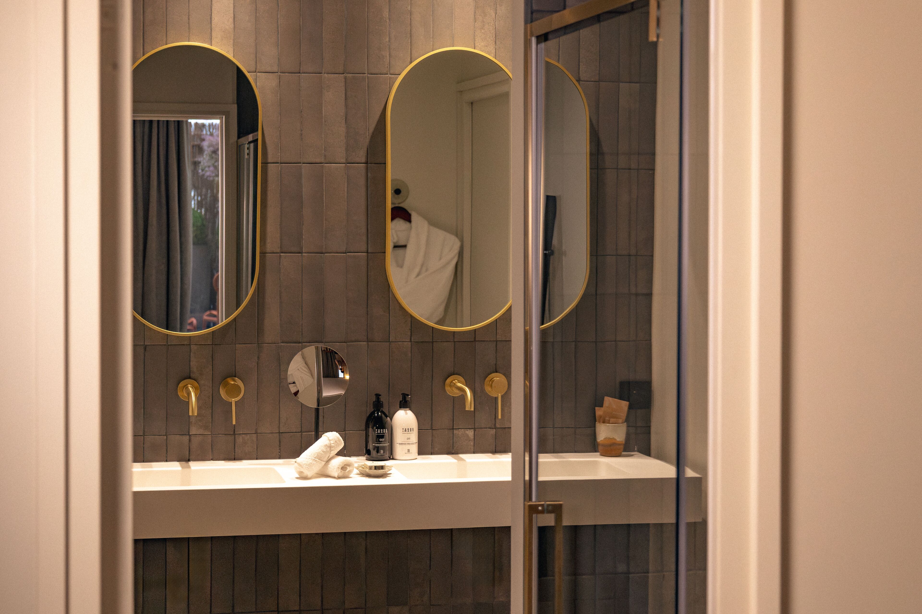 A modern bathroom with two oval mirrors, a white sink, and a towel rack.