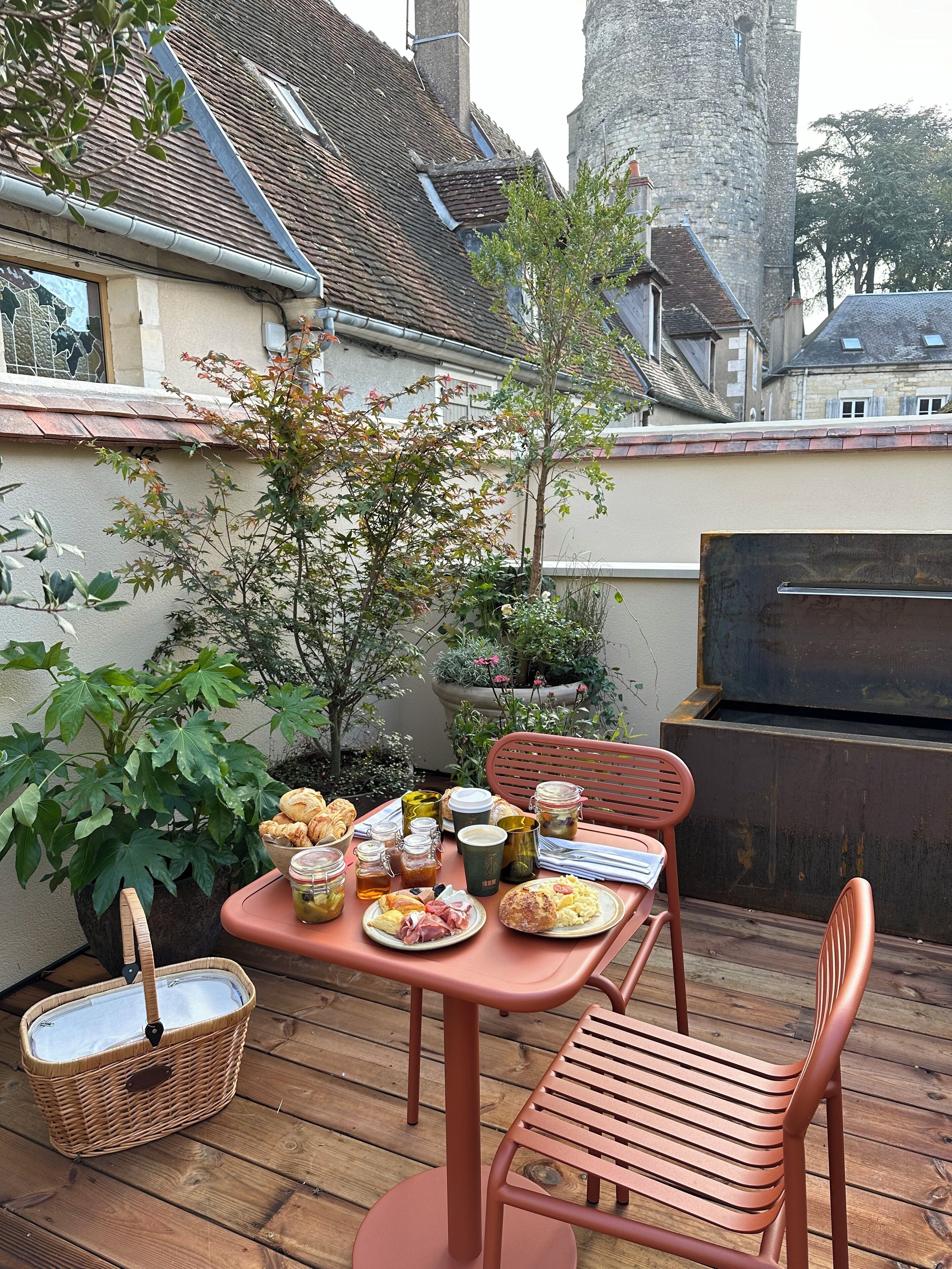 A patio with a table set for breakfast, including croissants, eggs, and coffee.
