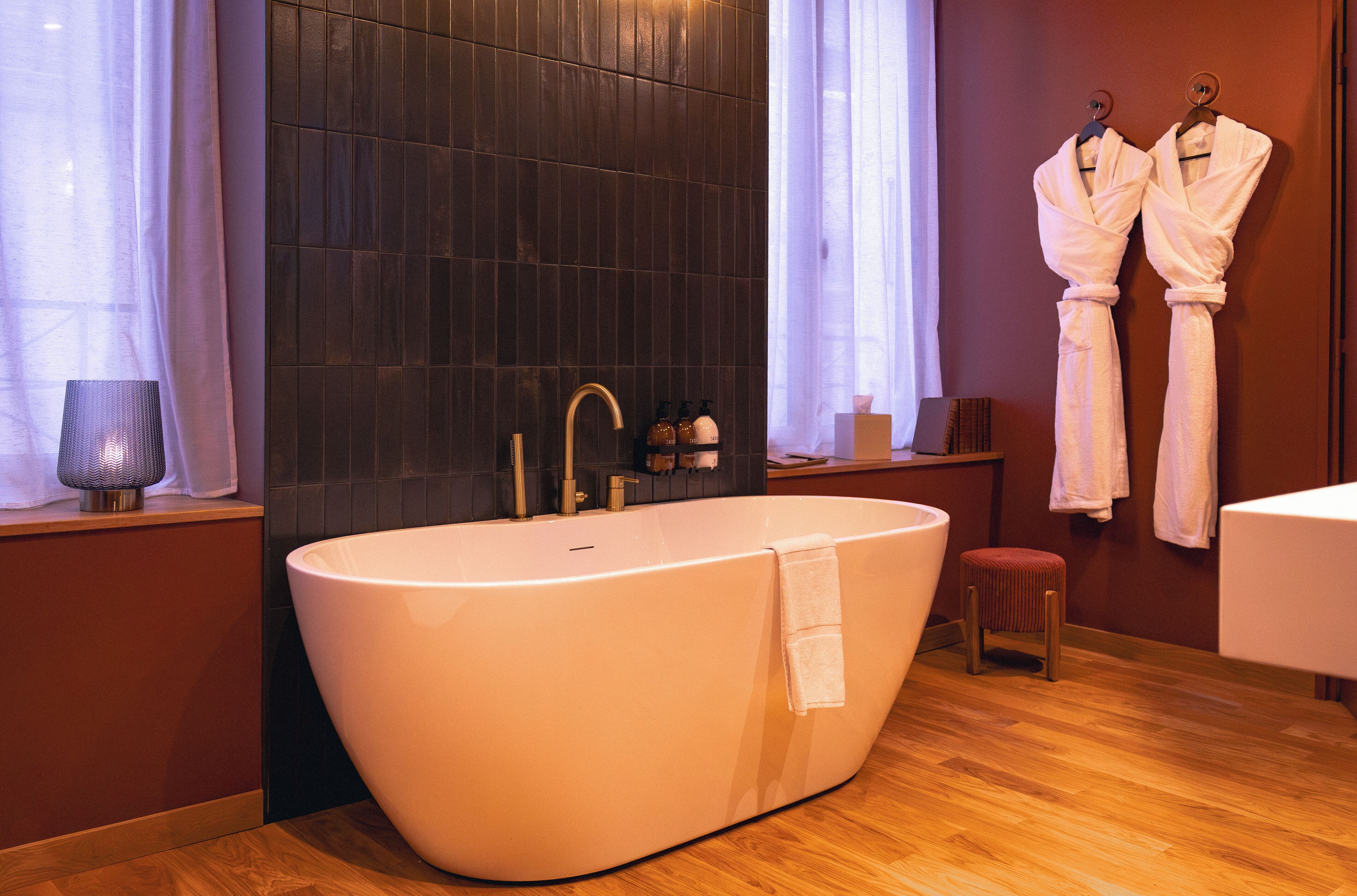 A modern bathroom with a freestanding bathtub, a wooden vanity, and two white robes hanging on hooks.