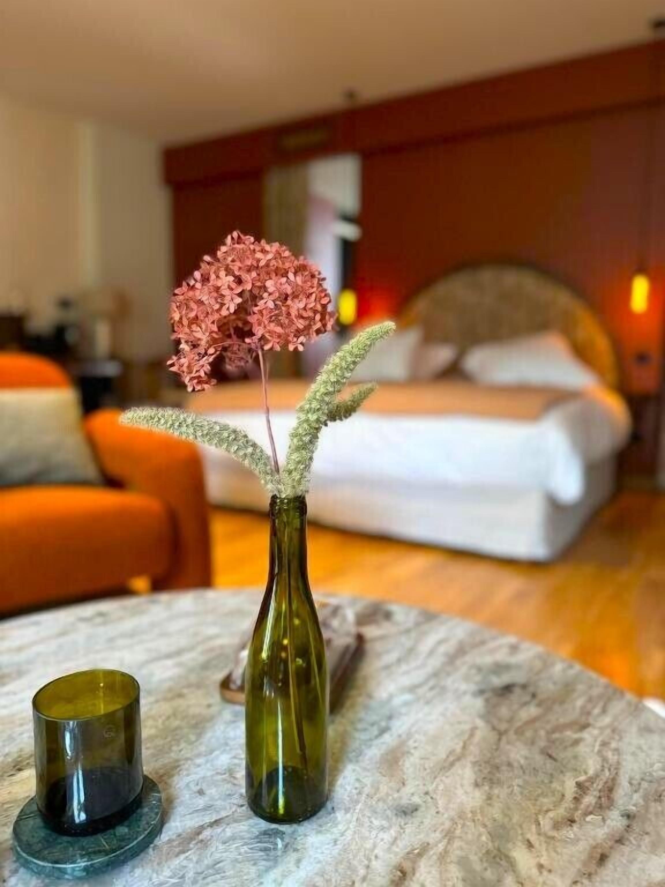 Ein Hotelzimmer mit einem Bett, einem runden Tisch mit Vase und Kerze sowie orangefarbenen Möbeln.