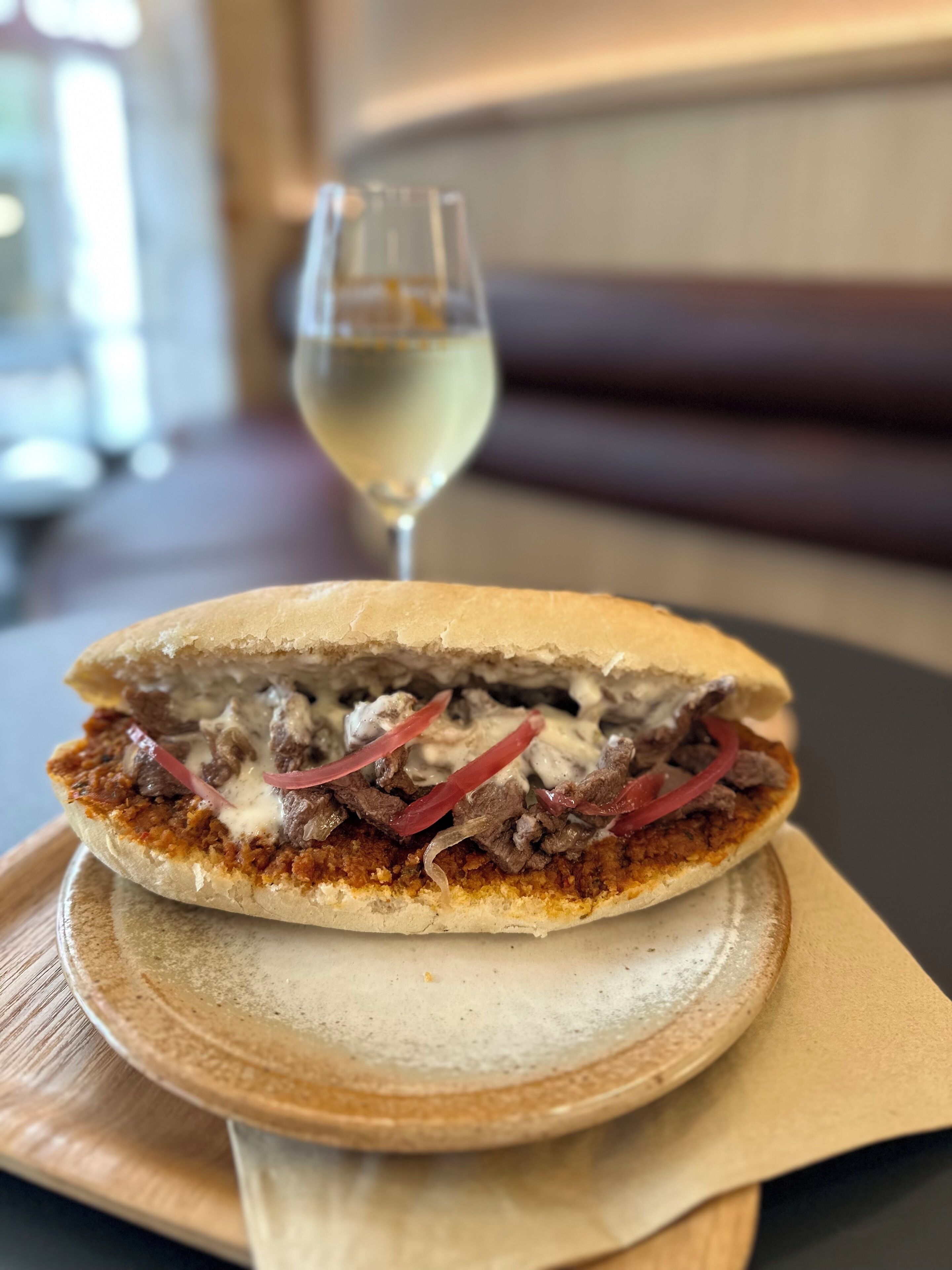 Sanduíche num prato, com um copo de vinho branco ao fundo.