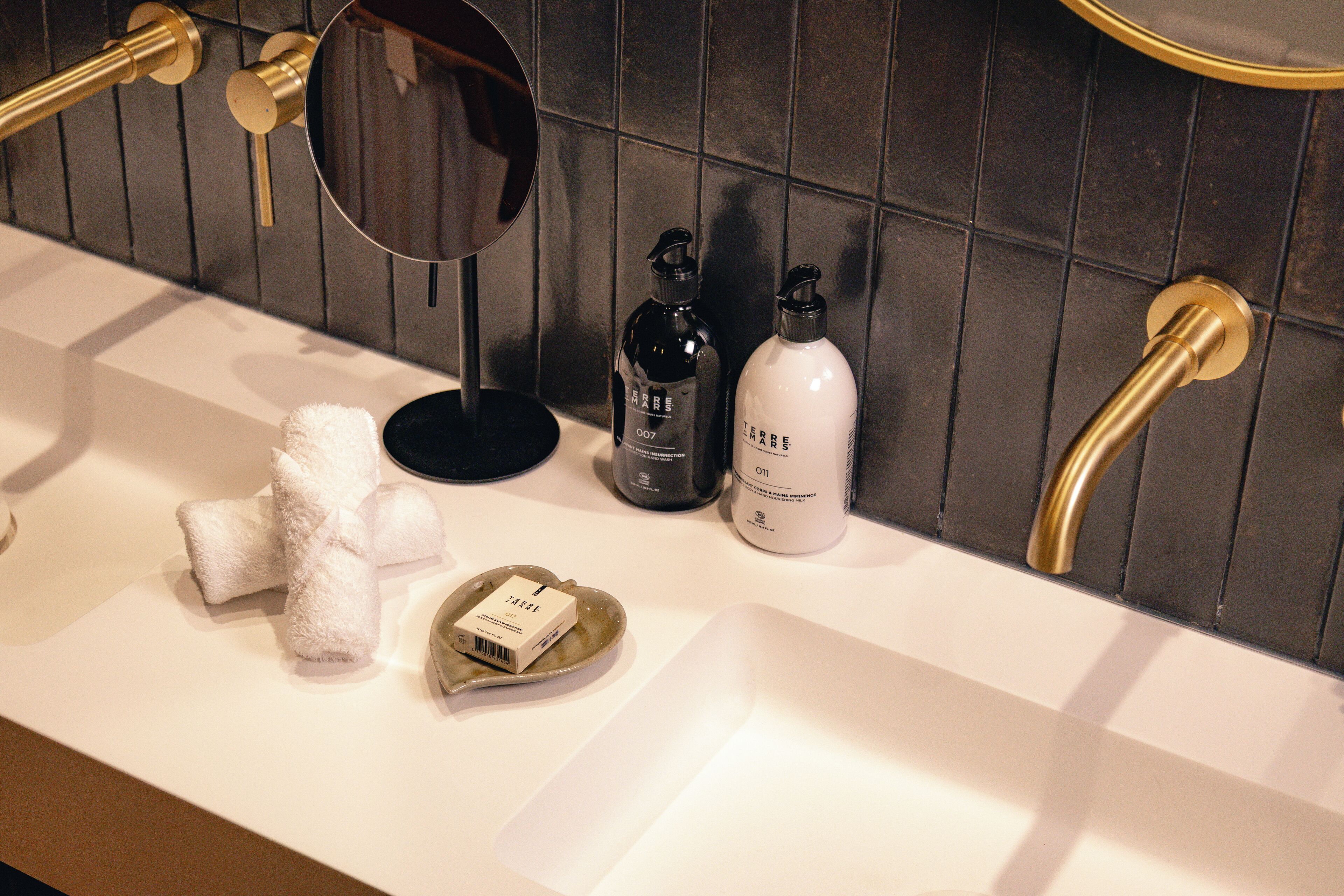 A bathroom with a white sink, gold fixtures, and a mirror. There are towels and two bottles on the counter.