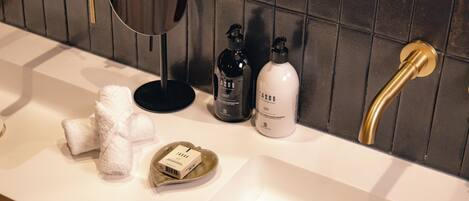 A bathroom with a white sink, gold fixtures, and a mirror. There are towels and two bottles on the counter.