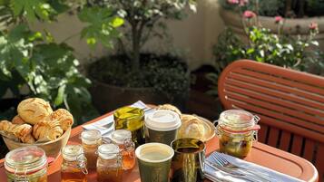 Tavolo apparecchiato all'aperto con diversi cibi per la colazione, tra cui pasticcini, uova e bevande.
