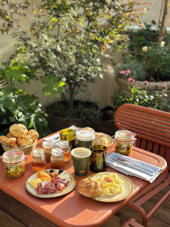 Une table dressée à l’extérieur, avec divers éléments pour le petit-déjeuner, notamment des viennoiseries, des œufs et des boissons.