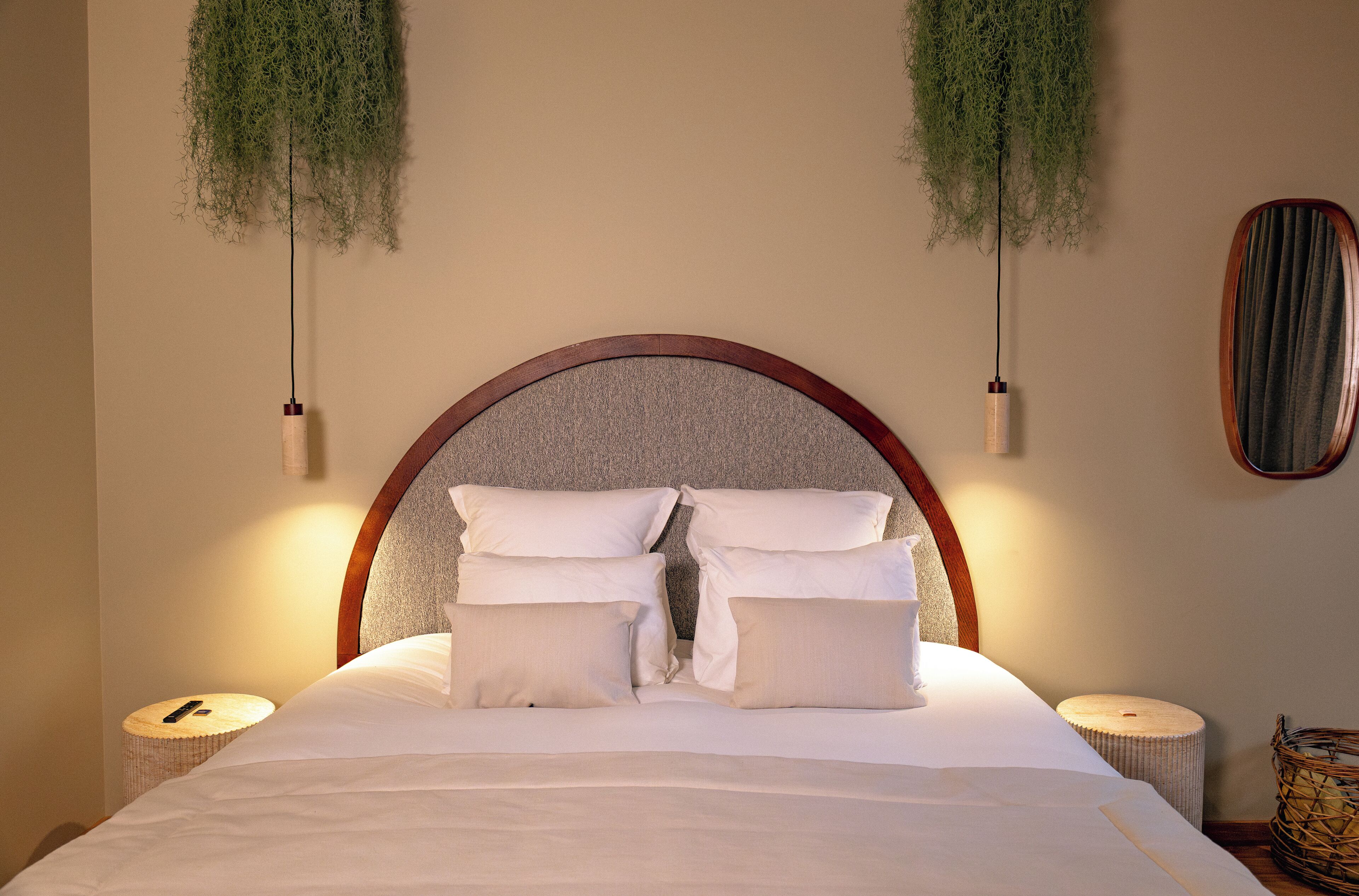 A neatly made bed with a wooden headboard, two bedside tables, and hanging greenery.