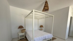 A white four-poster bed with a white headboard, two bedside tables with lamps, and a woven hanging light fixture. - Padel Resort 1bd Apartment (Raf Raf)