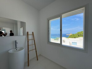 A bathroom with a large window, a sink, and a mirror.