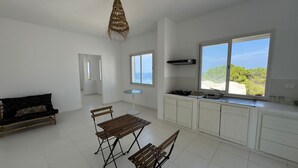 A spacious kitchen with white cabinets, a dining area with a bench, and a large window offering a view of the outdoors. - Padel Resort 1bd Apartment (Raf Raf)