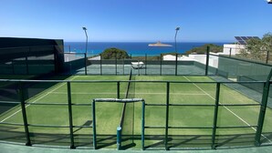 A tennis court with a net, surrounded by a green fence and solar panels. - Padel Resort 1bd Apartment (Raf Raf)