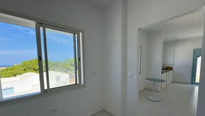 A spacious, modern room with a large window offering a view of the sea and greenery. - Padel Resort 1bd Apartment (Raf Raf)
